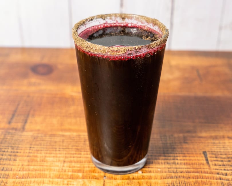 Dark red beverage in a glass with a golden-brown sugar rim, on a wooden table.