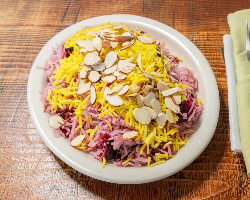 Colorful rice pilaf with yellow, pink, and dark grains, topped with sliced almonds on a white plate.