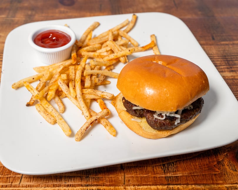 A burger with shredded cheese and a side of seasoned fries with ketchup on a white plate.