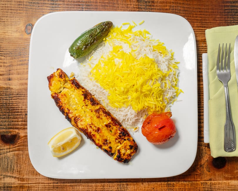 Grilled chicken kebab with saffron rice, roasted tomato, and jalapeño on a white plate.